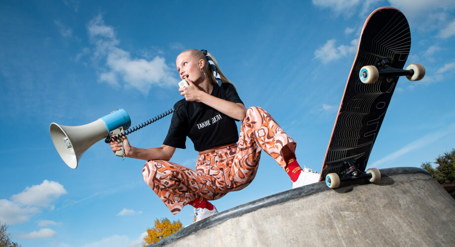 «Девушка в футболке „Такие дела“ с мегафоном и скейтом на бетонном блоке»